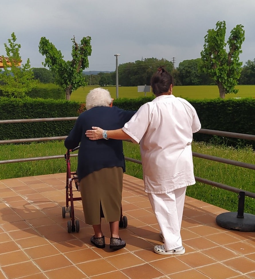 mujer mayor y su cuidadora paseando por la terraza de la residencia