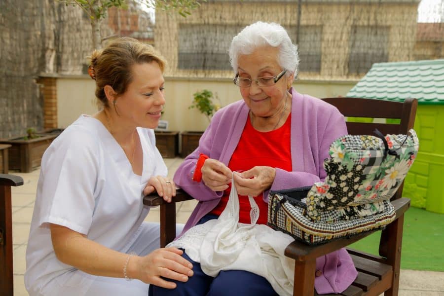 mujer mayor tejiendo junto a su cuidadora